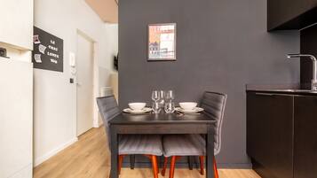 Un comedor moderno con una mesa de madera oscura dispuesta para dos, sillas grises con tapicería y un cuadro en la pared.