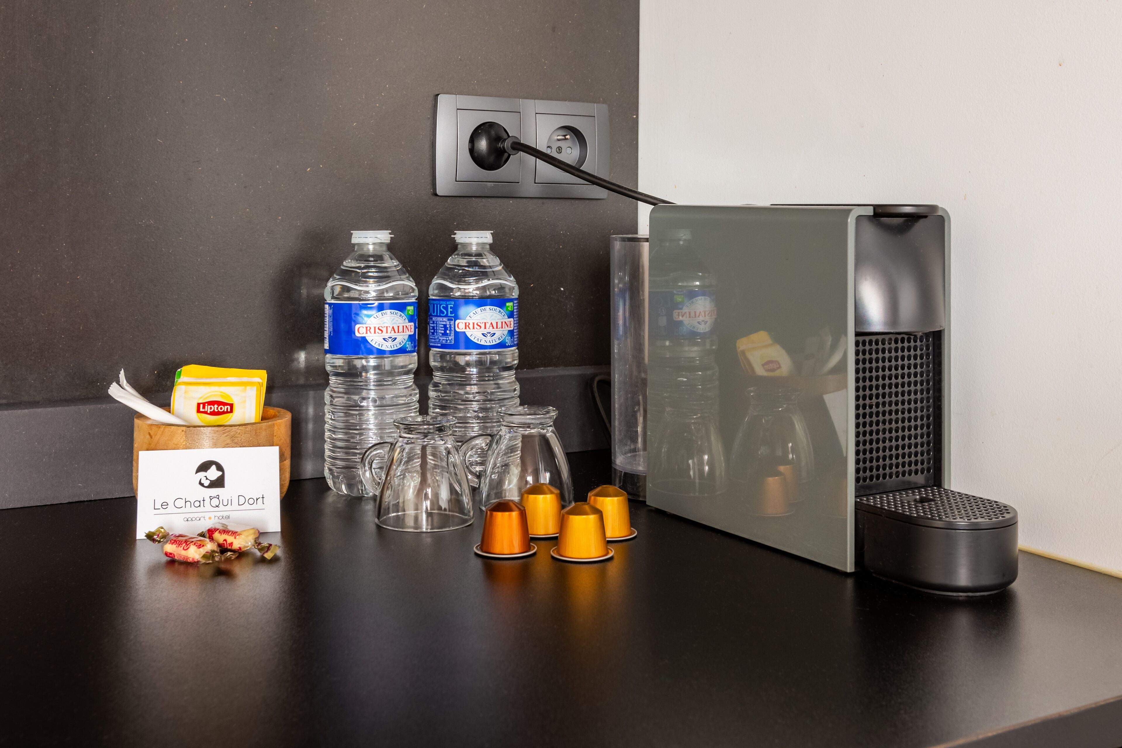 Un comptoir de cuisine avec une machine à café, des bouteilles d’eau, une tasse à café et une boîte de thé Lipton.