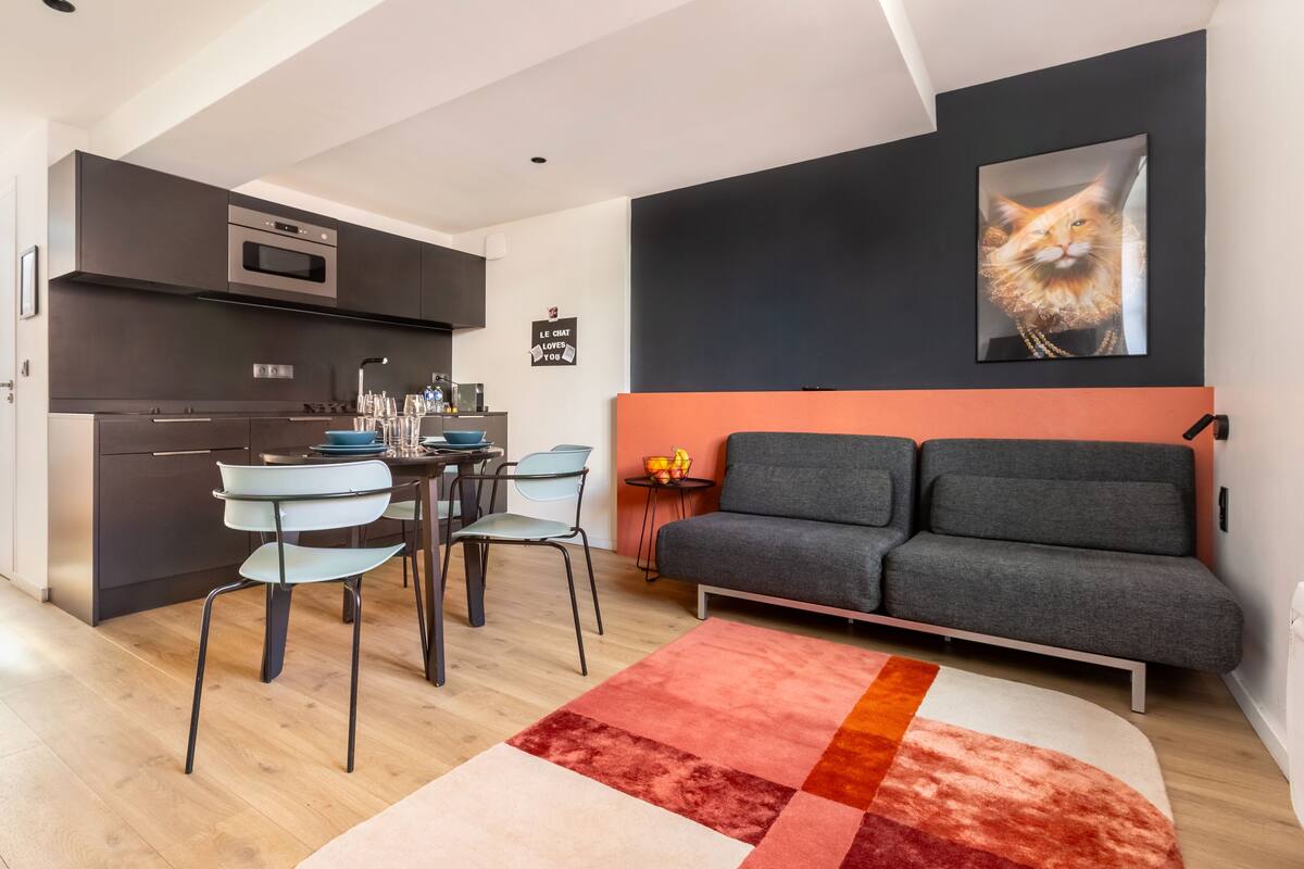 Une cuisine moderne avec des meubles de couleur sombre, un four encastré et un coin repas comprenant une table et des chaises.