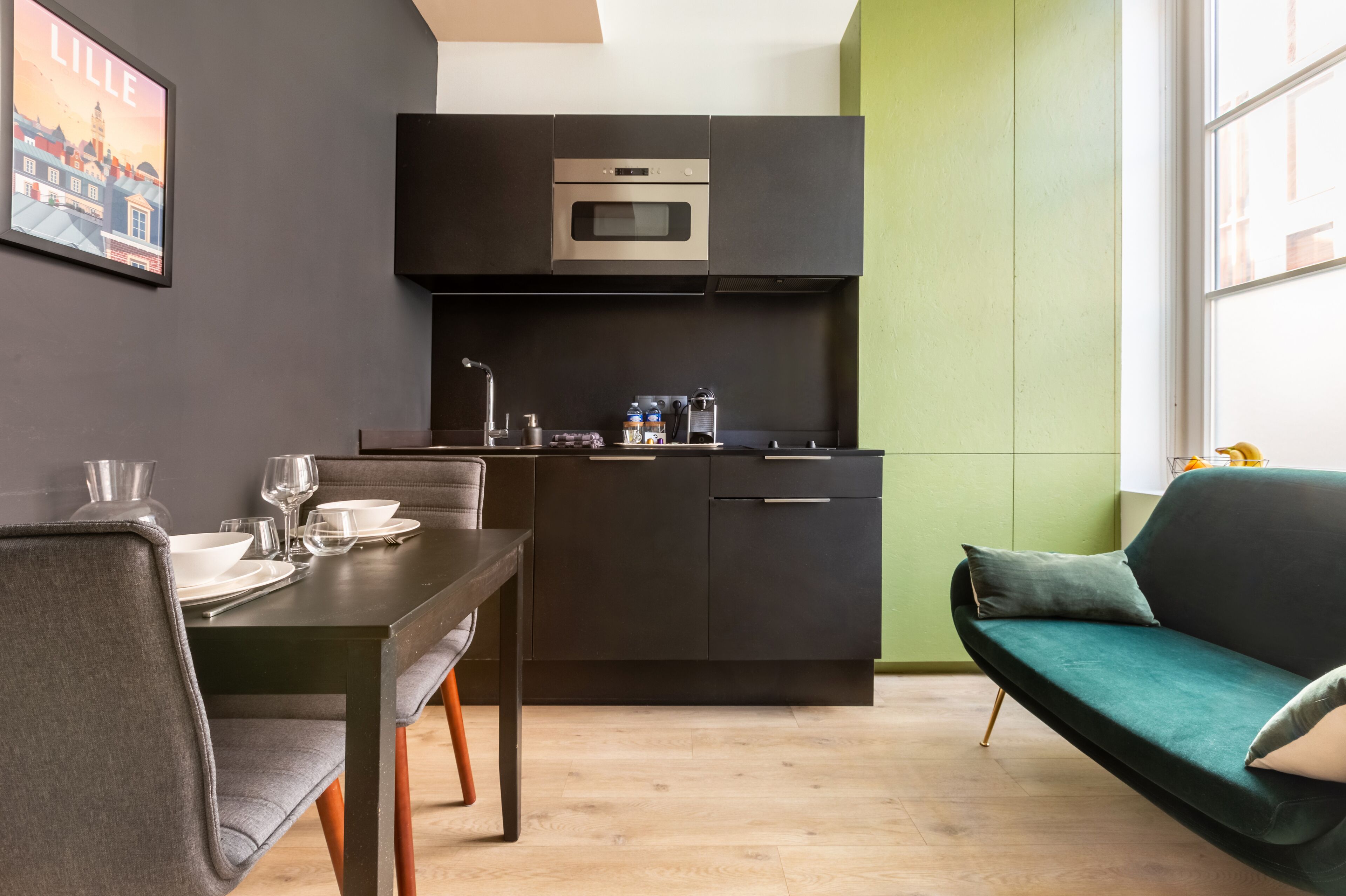 A modern kitchen with dark cabinetry, a built-in oven, and a dining area with a table set for two.