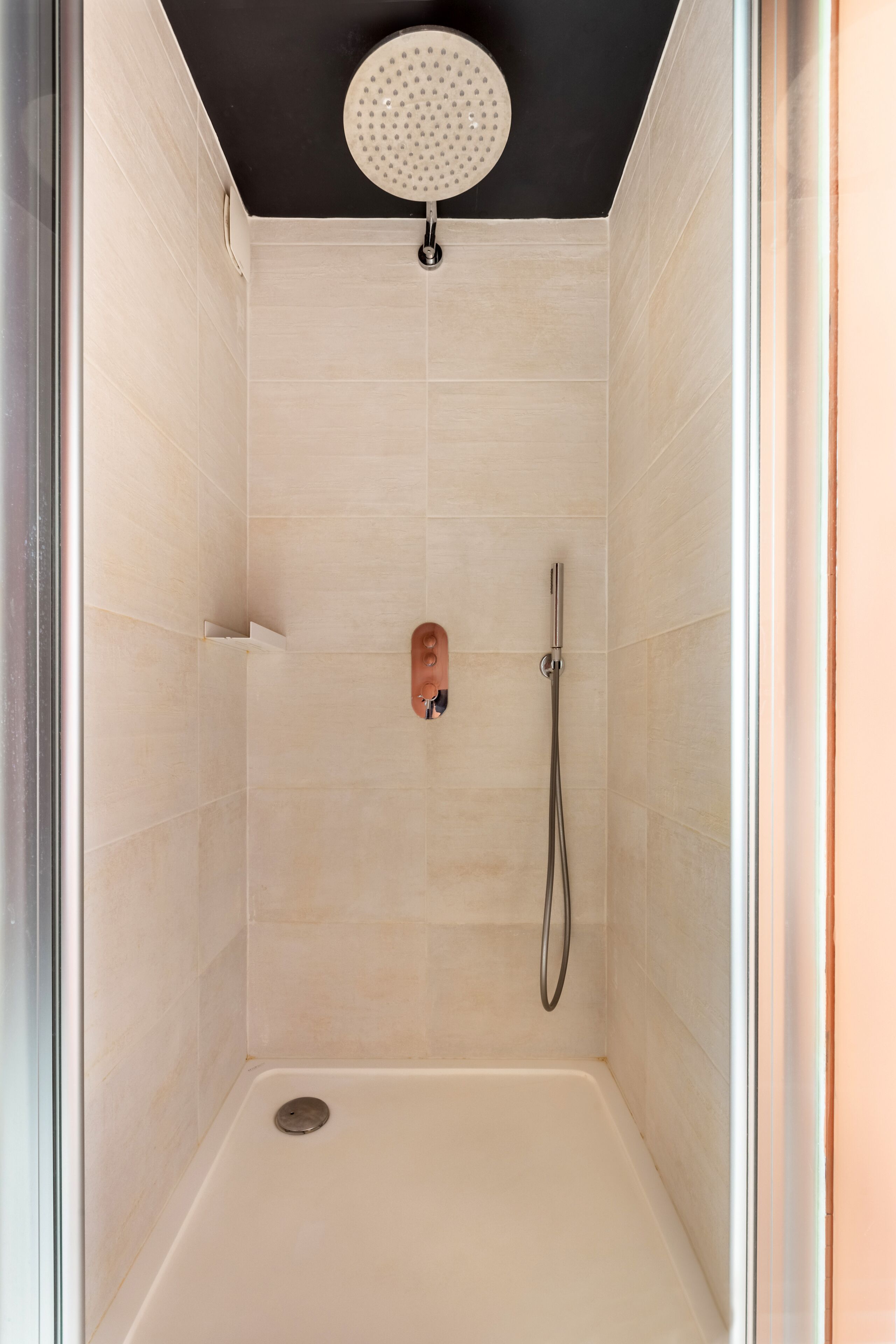 A walk-in shower with a handheld showerhead, a handheld showerhead, and a drain.