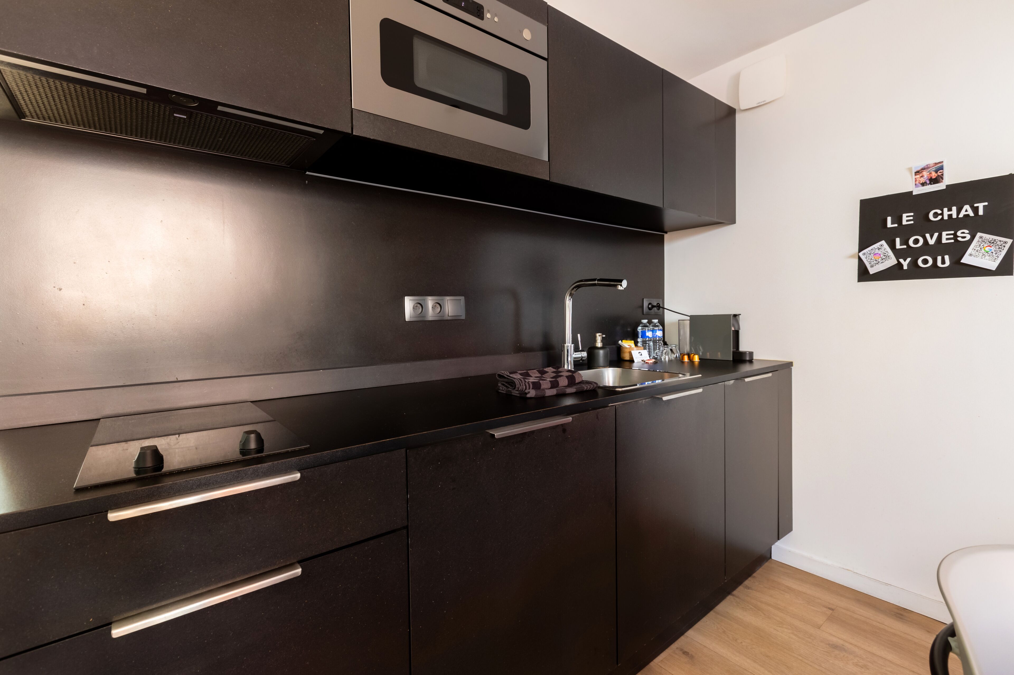 A modern kitchen with dark cabinetry, a stainless steel oven, and a wall-mounted light.