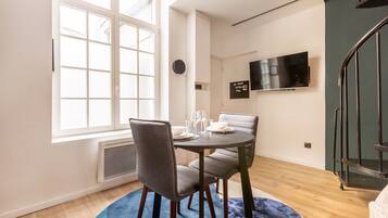 A dining area with a round table, two chairs, a window, a flat-screen TV, and a staircase.