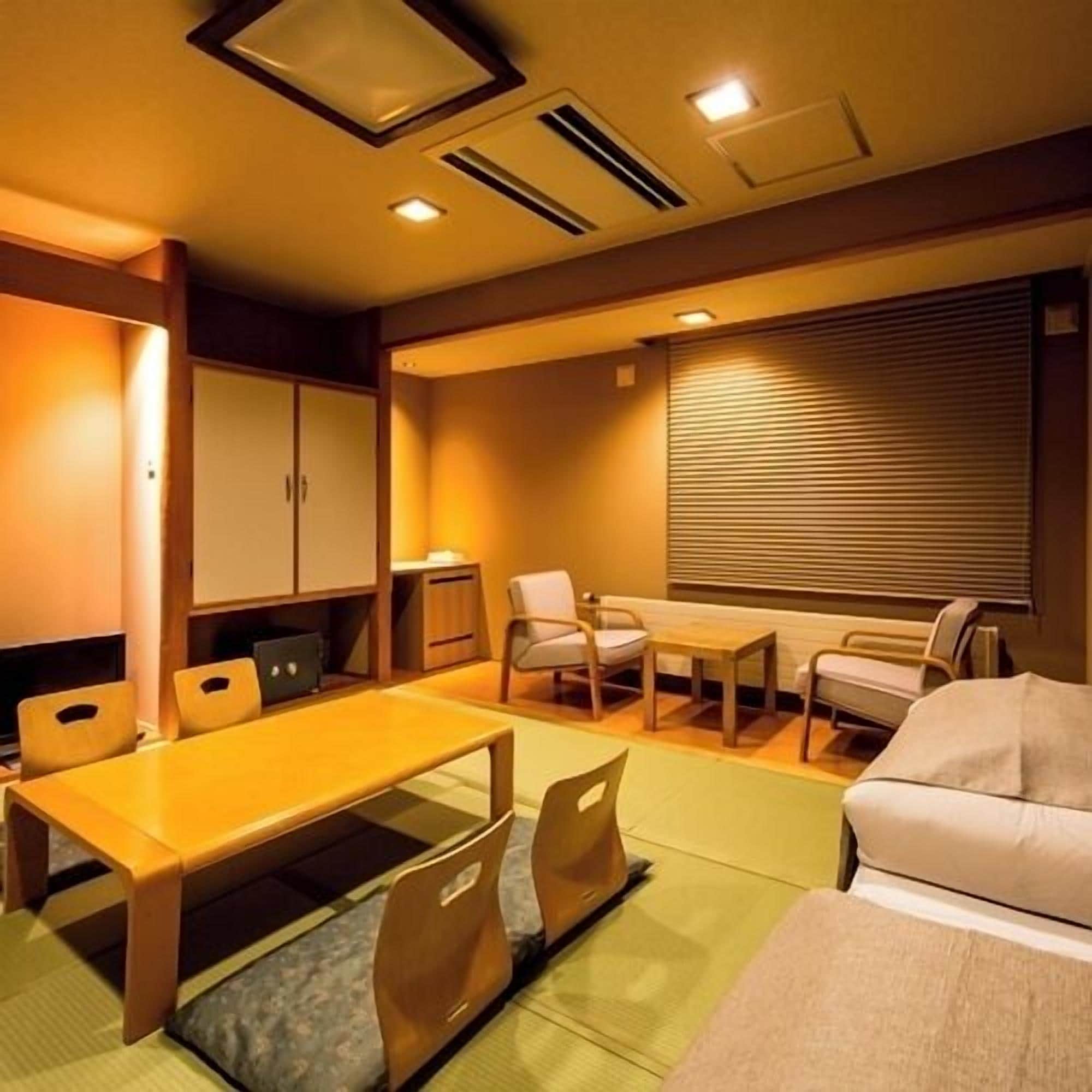 Quarto de hotel com mesa de jantar, cadeiras, sofá e janela com persianas.