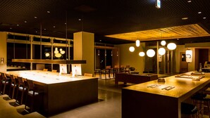 A modern restaurant with a central island, multiple seating areas, and pendant lighting. - Hatagoya Jyozankei Shoten - Hostel (Sapporo)
