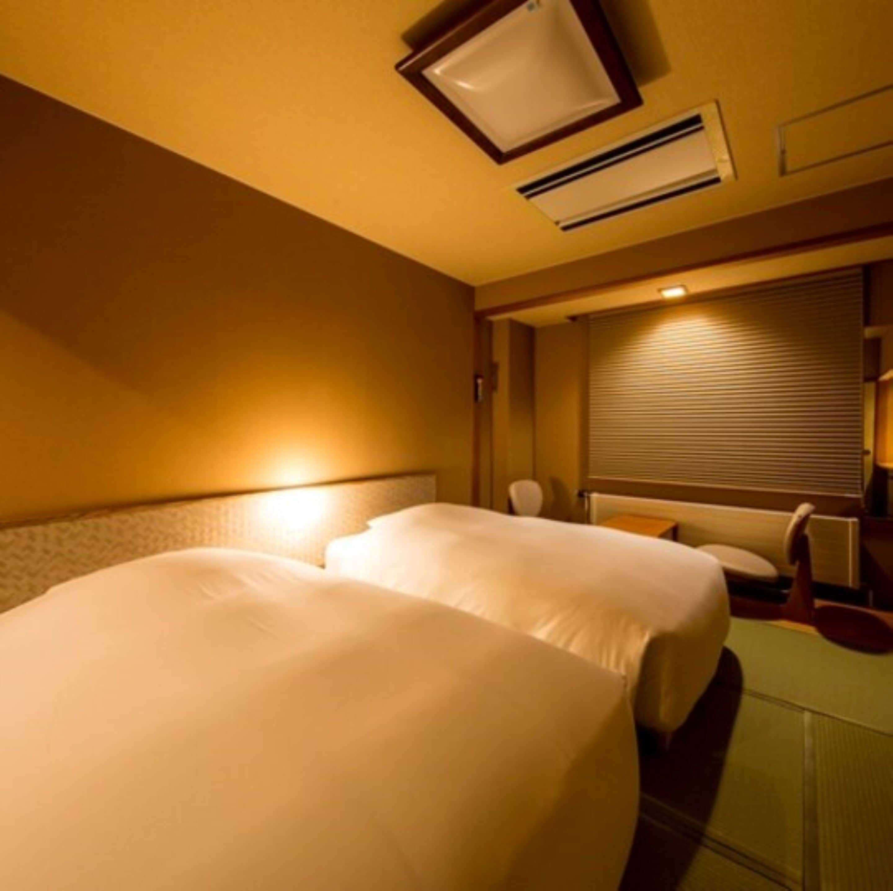 Une chambre d’hôtel avec deux lits, un bureau et une fenêtre avec des stores.