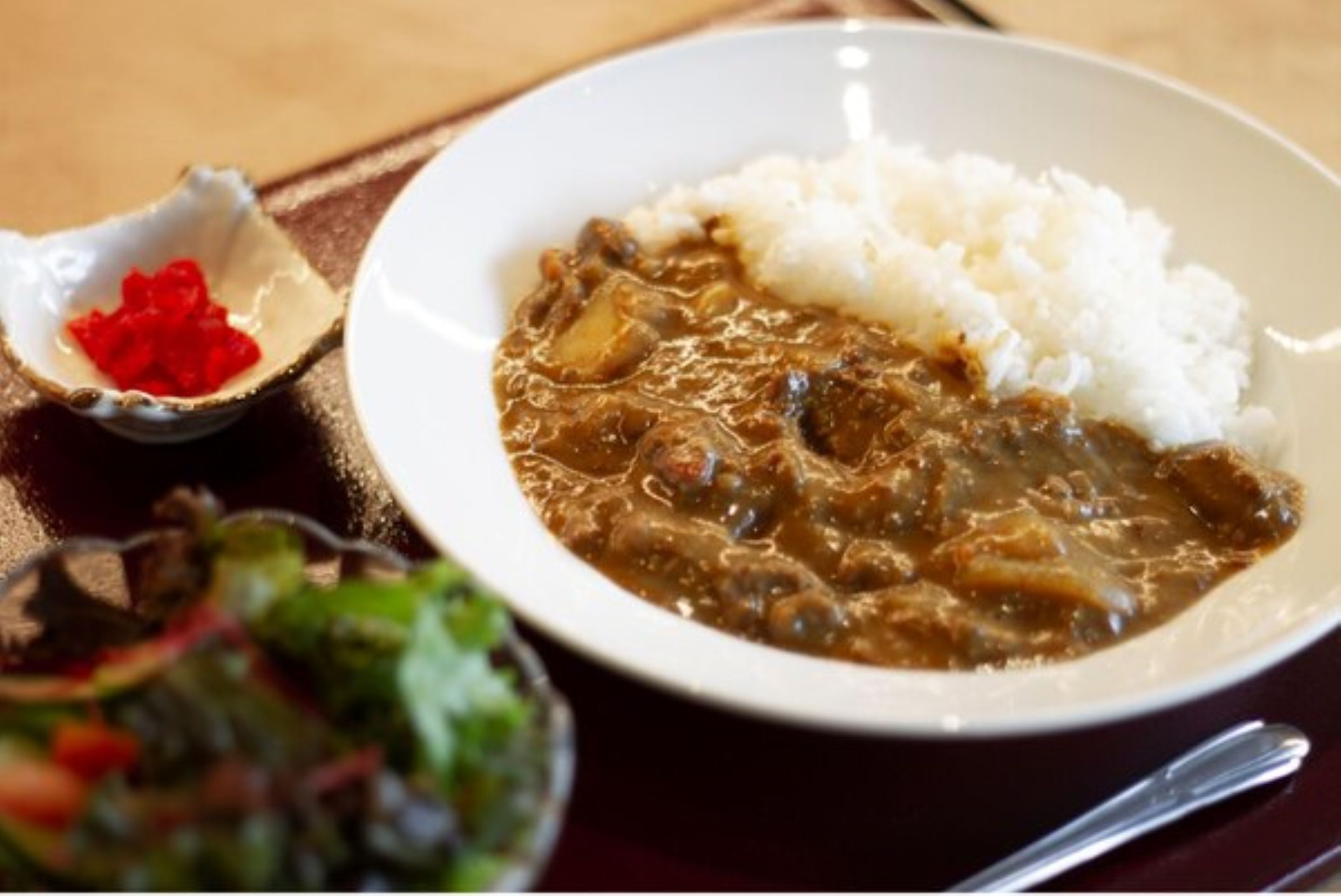 A plate of curry with rice and a small bowl of red sauce.