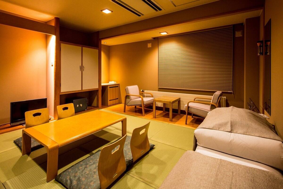 A traditional Japanese room with tatami flooring, a low table, chairs, a sofa, and sliding doors.