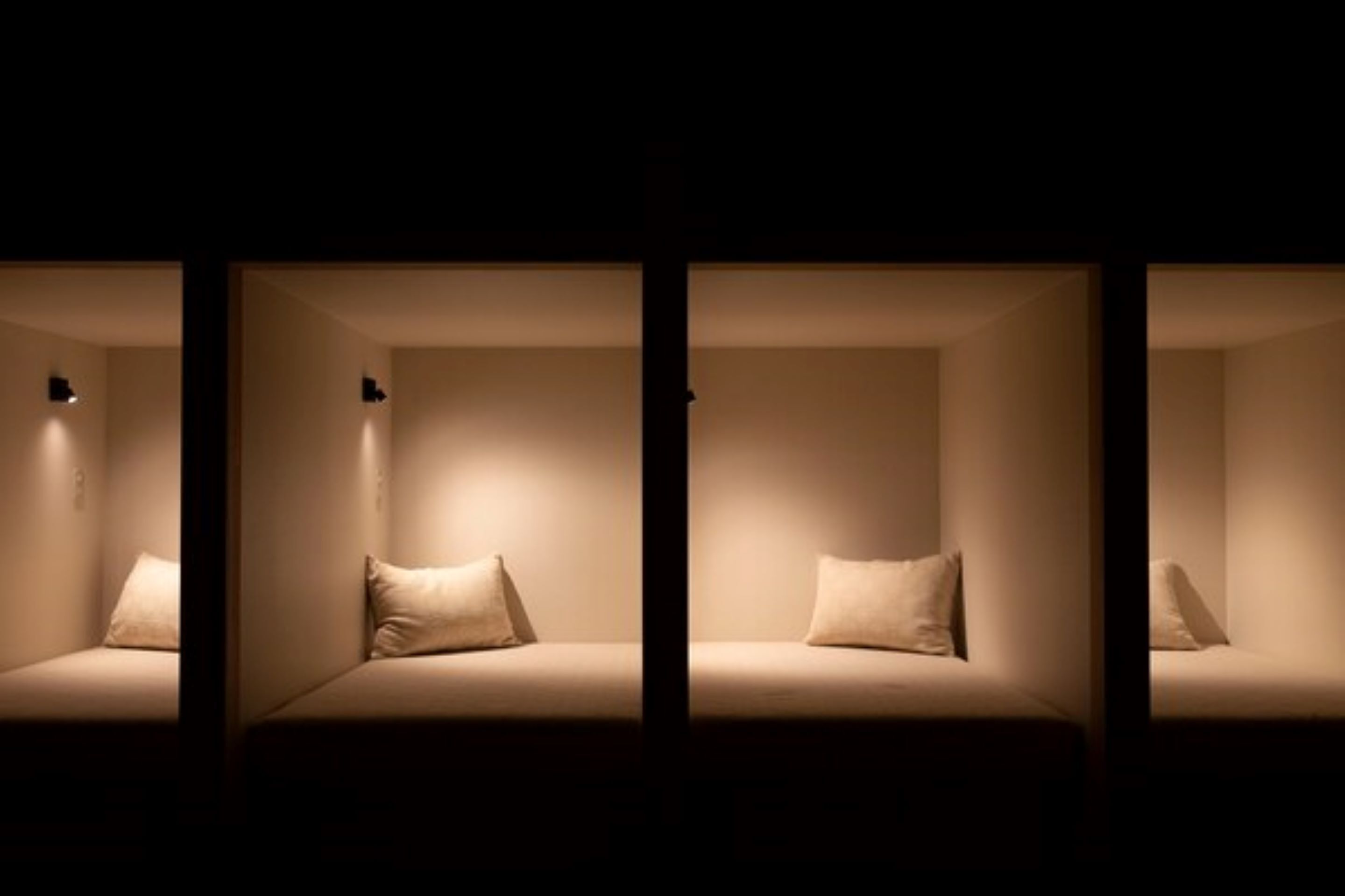 Una serie di tre camere con un design minimalista, ognuna con un letto singolo e un piccolo comodino.