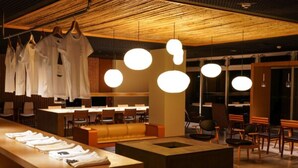 A modern restaurant interior with hanging white shirts, round pendant lights, and a long counter with folded shirts. - Hatagoya Jyozankei Shoten - Hostel (Sapporo)