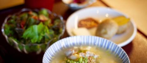 A bowl of soup with green onions and meat, a plate with dumplings, and a bowl of salad.
