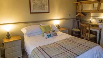 A neatly made bed with a plaid blanket, two bedside tables with lamps, a wooden chair, and a map on the wall.