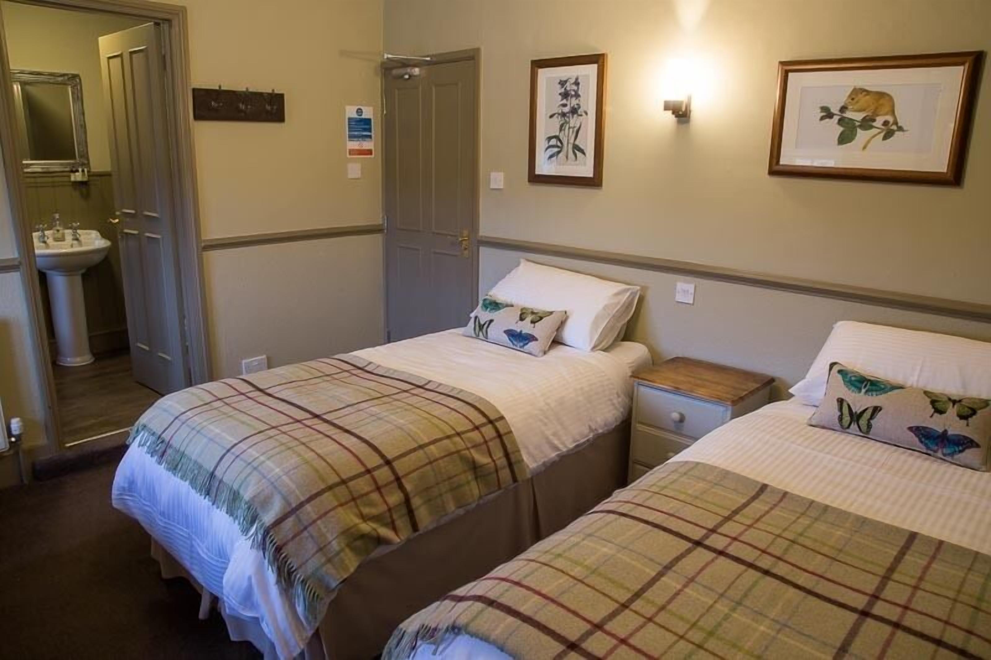 Ein Hotelzimmer mit zwei Betten, einem Nachttisch, einem Waschtisch und Spiegeln. An den Wänden befinden sich gerahmte Kunstwerke.