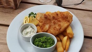 Une assiette contenant du poisson-frites, des quartiers de citron et deux petits ramequins de sauces d'accompagnement.