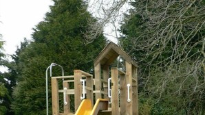 Une structure de jeux en bois, dotée d’un toboggan jaune et d’éléments d’escalade.