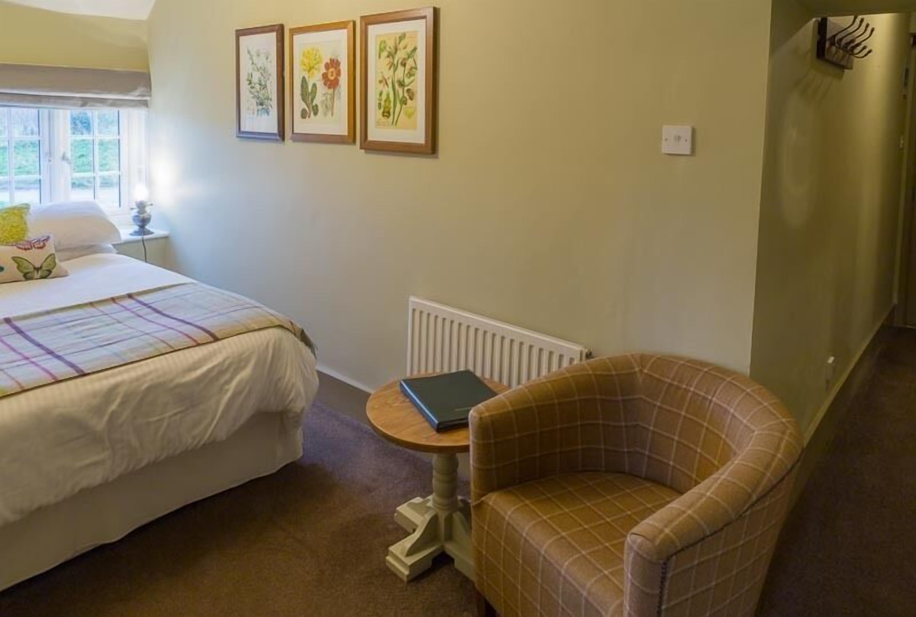 Une chambre à coucher avec un lit, une chaise, une petite table sur laquelle se trouve un livre, et trois tableaux représentant des motifs floraux, accrochés au mur.