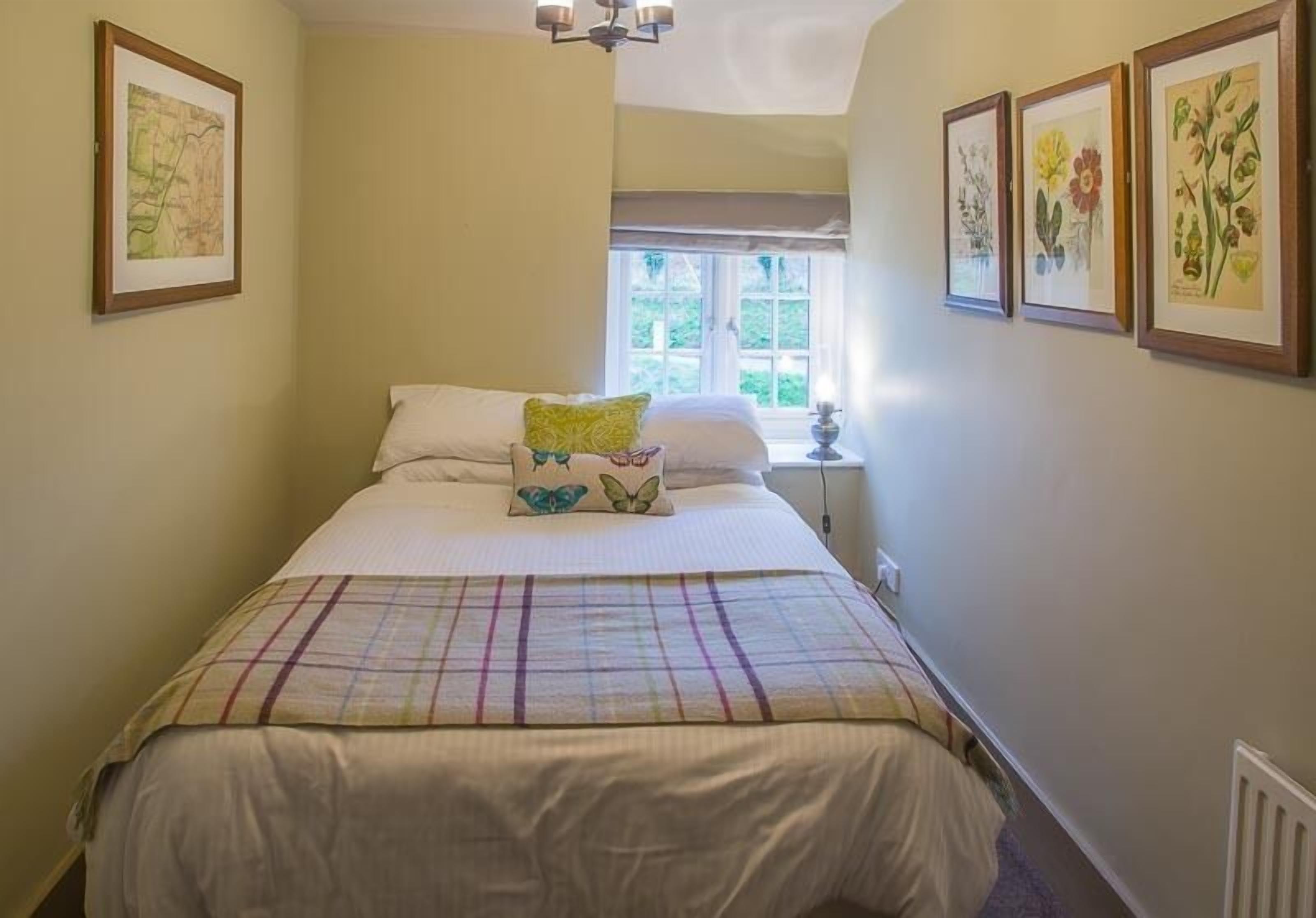 A bedroom with a bed, a window, and framed botanical prints on the wall.