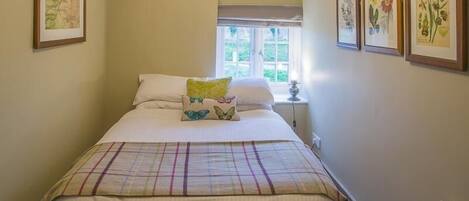 A bedroom with a bed, a window, and framed botanical prints on the wall.