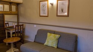 Une pièce chaleureuse avec un canapé gris, une chaise en bois, une petite table ronde et deux reproductions botaniques encadrées accrochées au mur.