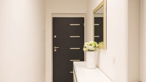 Un couloir avec une porte noire, une console blanche ornée d’un vase de fleurs et un miroir accroché au mur.