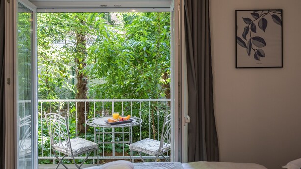 Une chambre avec un lit, un balcon avec une table et des chaises, et une vue sur la verdure environnante.