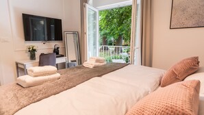 Une chambre d’hôtel avec un grand lit, un bureau avec une chaise, une télévision et un balcon donnant sur la verdure.