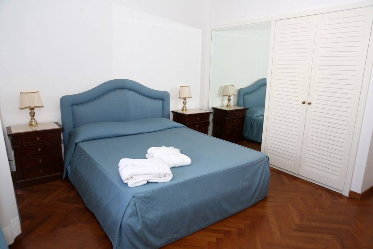 Un dormitorio con una cama individual, dos mesitas de noche con lámparas, un armario y un espejo.