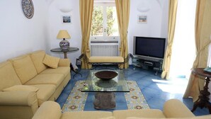 A living room with a sofa, a glass coffee table, a TV, and a small table with a lamp. - La Cicas (Anacapri)