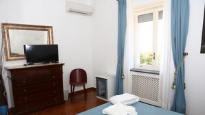 A bedroom with a bed, a dresser, a chair, a television, and a window with curtains. - La Cicas (Anacapri)