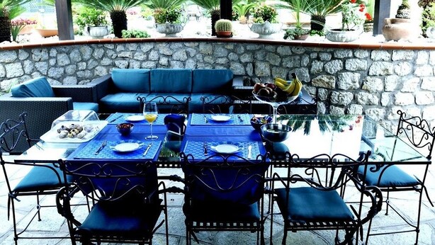 An outdoor patio with a stone wall, blue seating, and potted plants. - La Cicas (Anacapri)