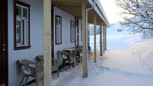 A snow-covered outdoor area with a wooden structure, including a porch with chairs and a table. - Sel Guesthouse (Selfoss)
