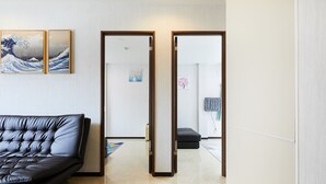 Una sala de estar moderna con un sofá de cuero negro, un espejo con marco de madera y una obra de arte tradicional japonesa en la pared.