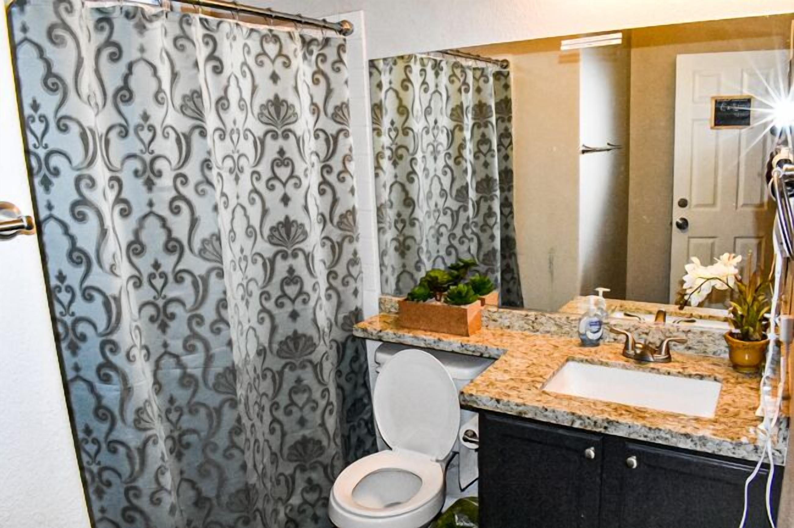 A bathroom with a shower curtain, toilet, sink, and a small potted plant.