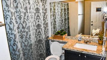 A bathroom with a shower curtain, toilet, sink, and a small potted plant.