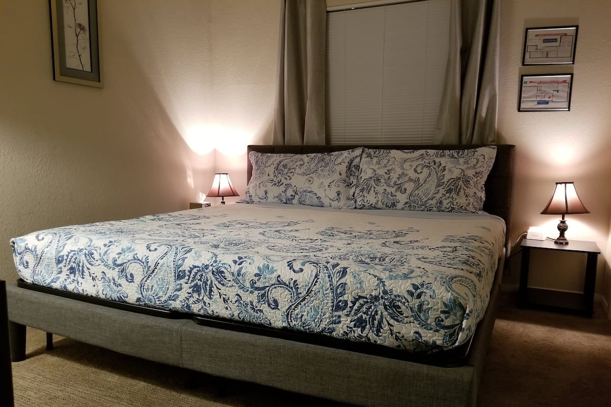 A neatly made bed with a patterned bedspread, two bedside lamps, and a framed map on the wall.