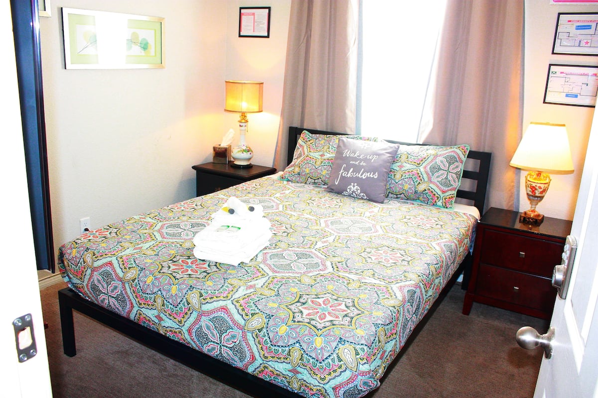 A neatly made bed with a patterned bedspread, a pillow with a motivational quote, and a bedside table with a lamp.
