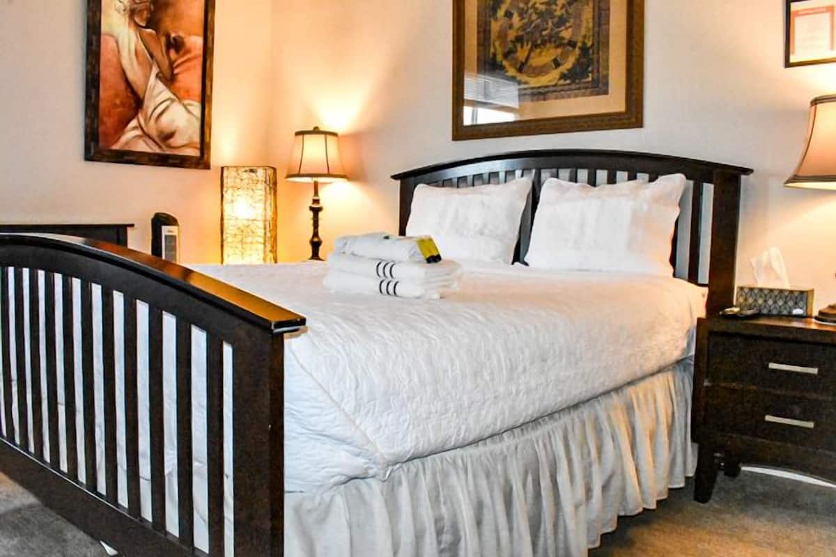 A neatly made bed with white linens, a wooden headboard, and a bedside table with a lamp.
