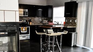 A modern kitchen with dark wood flooring, a built-in oven, a microwave, and a large island with bar stools. - Advantage Court (Las Vegas)