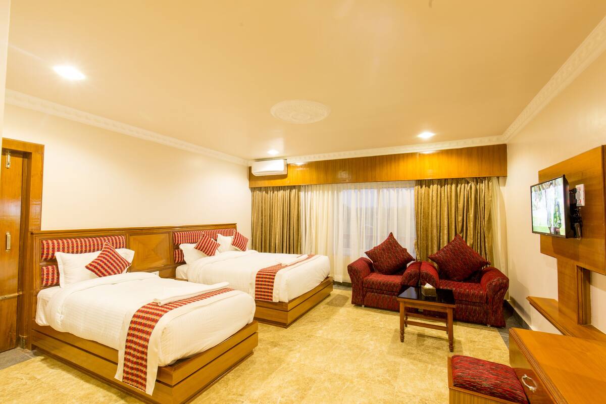 A hotel room with two beds, a sofa, a TV, and a desk.