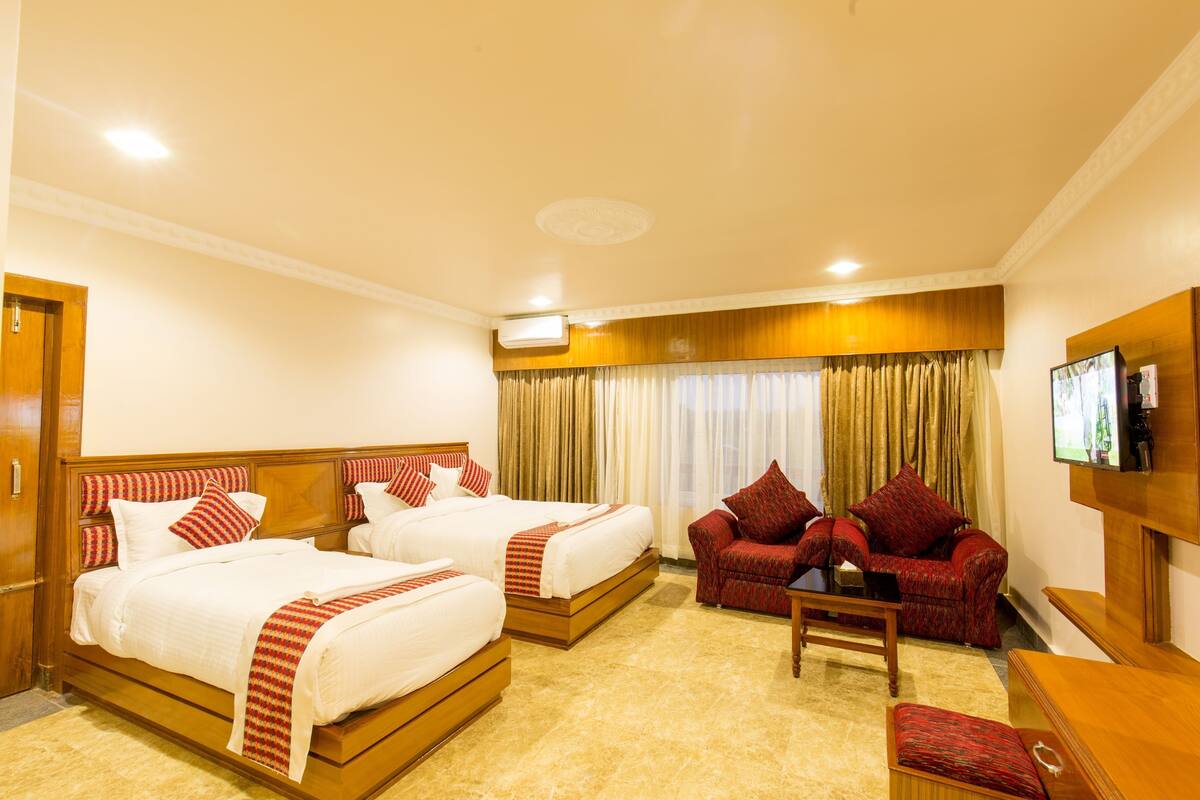 A hotel room with two beds, a sofa, a TV, and a wooden cabinet.
