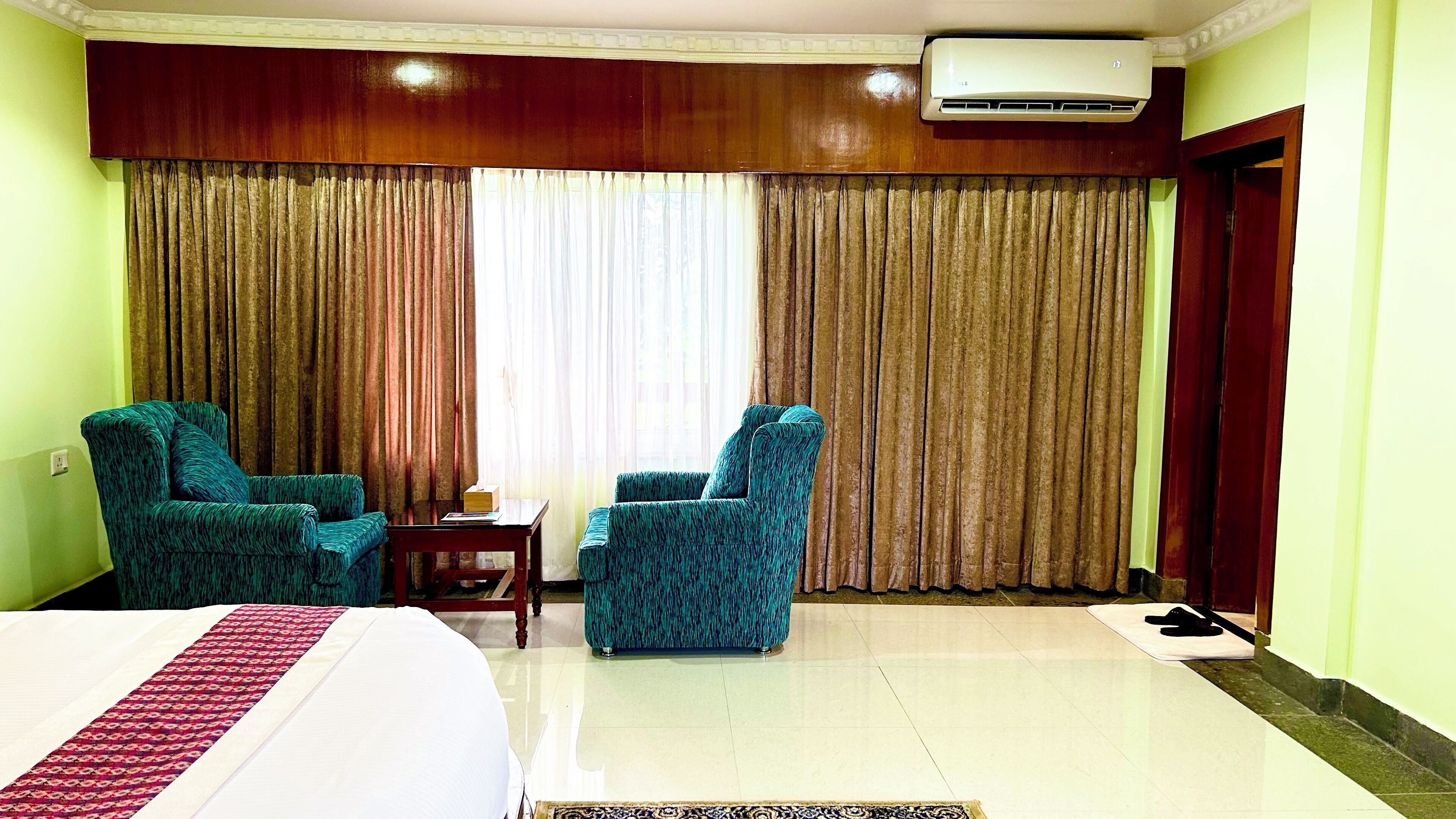 A hotel room with a bed, two armchairs, a small table, and a large window with curtains.