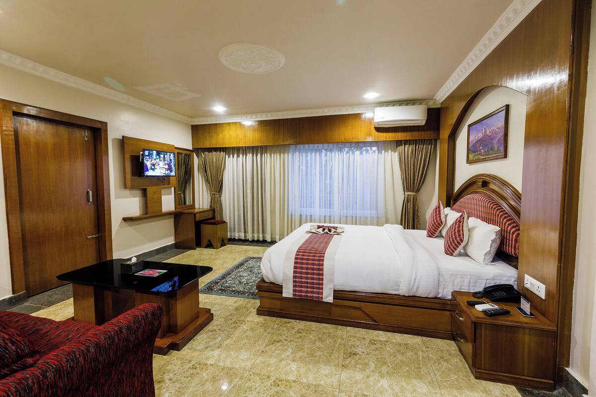 A hotel room with a bed, a TV, a desk, and a red armchair.