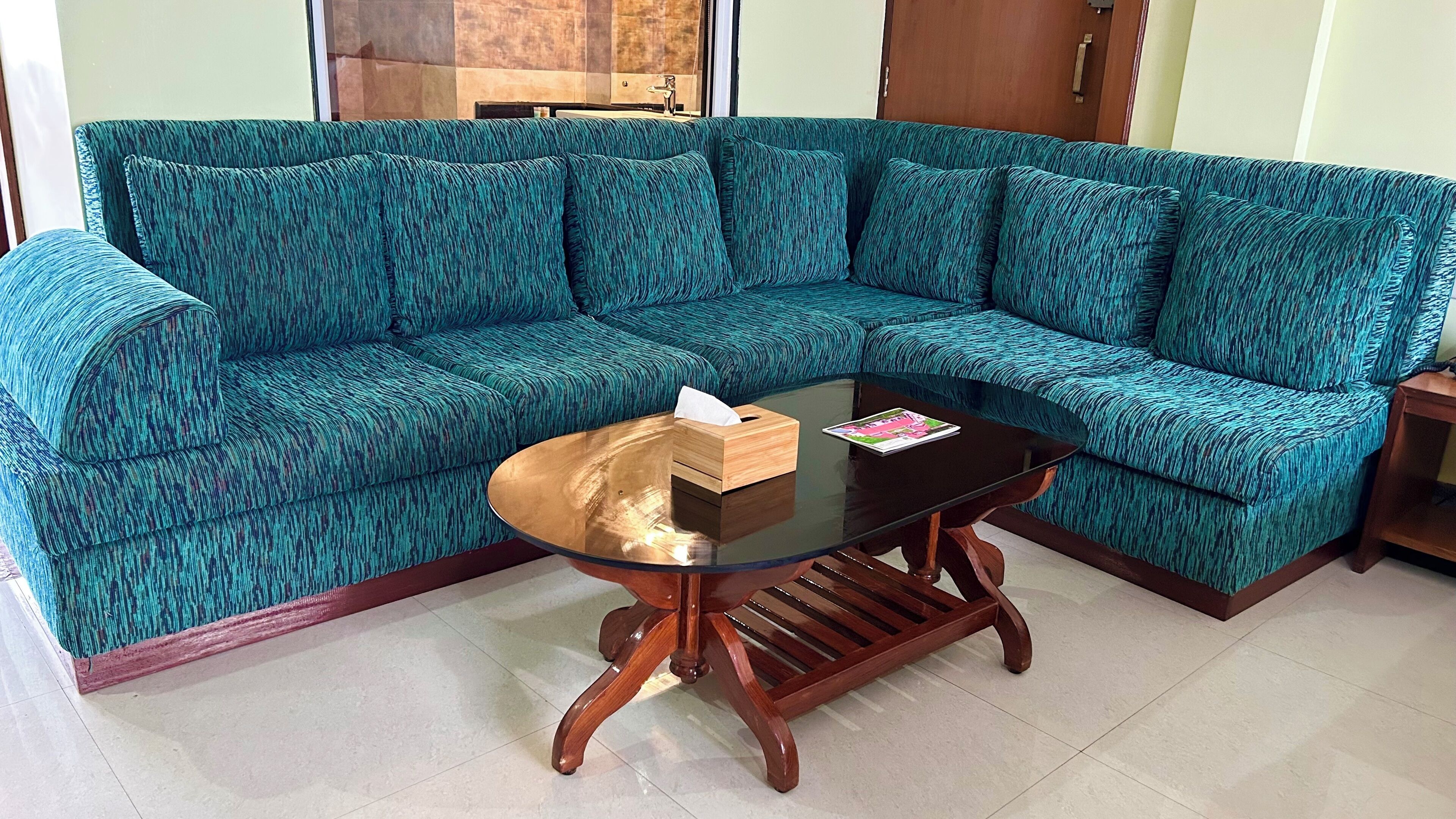 A teal patterned sofa with a glass coffee table and a tissue box.