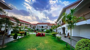 A courtyard with a lawn, potted plants, and a dining area with red chairs. - Hotel Earth Light (Sauraha)