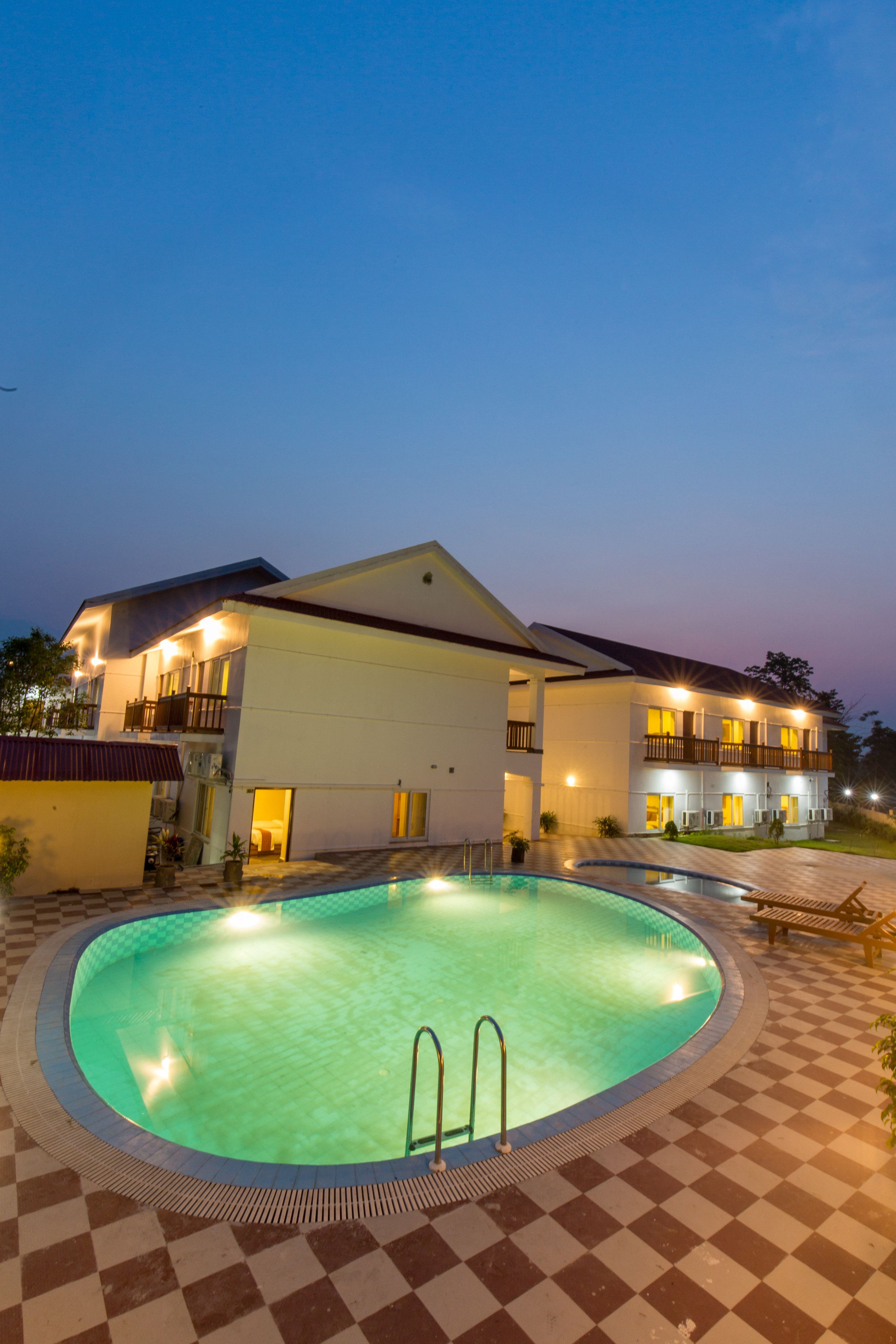A hotel with a swimming pool, a checkered floor, and a well-lit exterior at dusk.
