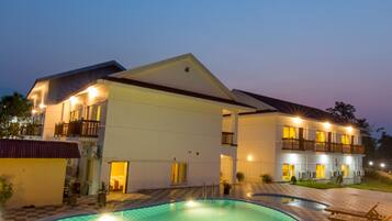 A hotel with a swimming pool, a checkered floor, and a well-lit exterior at dusk.