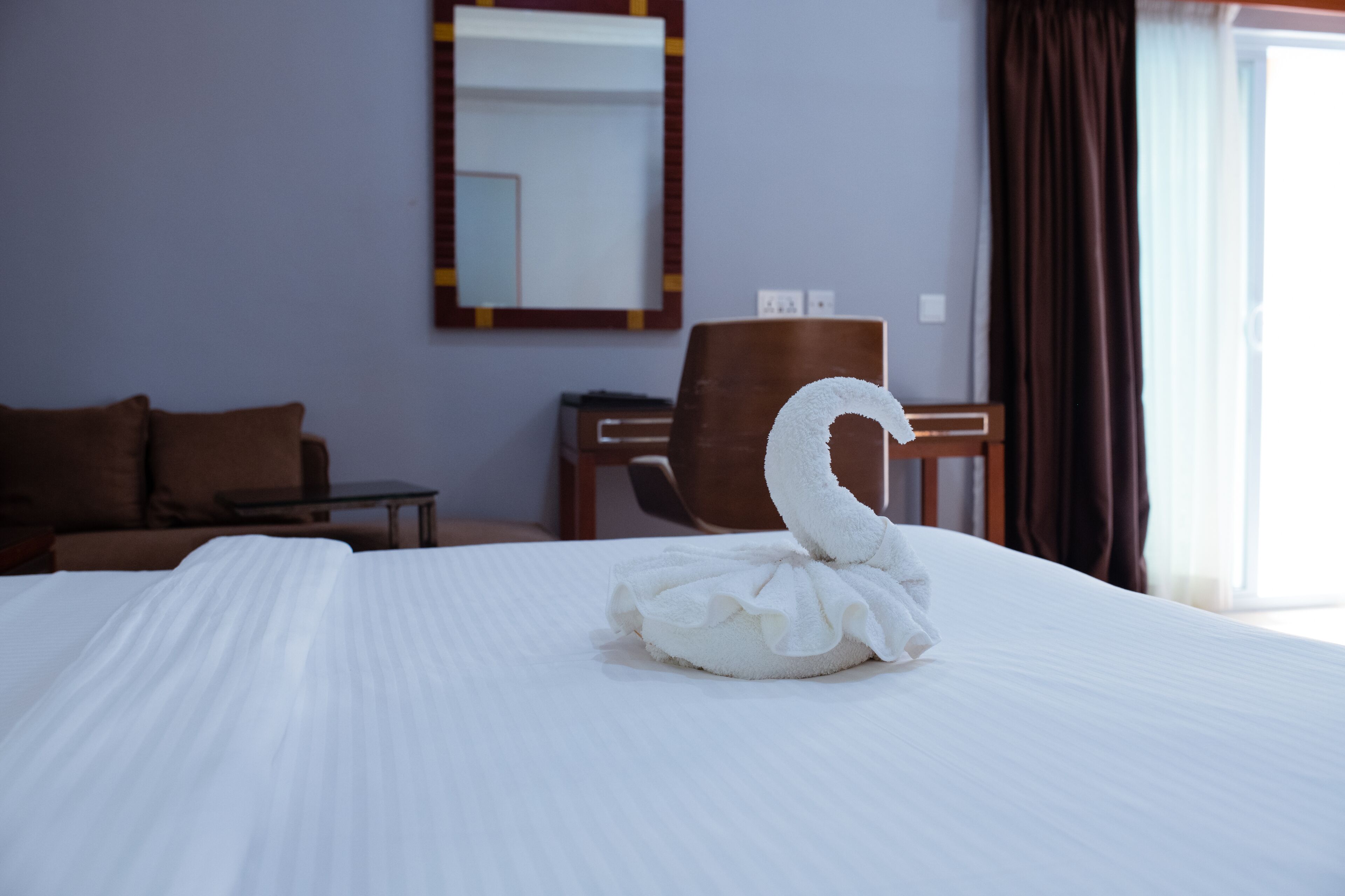 Una habitación de hotel con una cama bien hecha, una silla de madera, una mesita y un espejo en la pared.