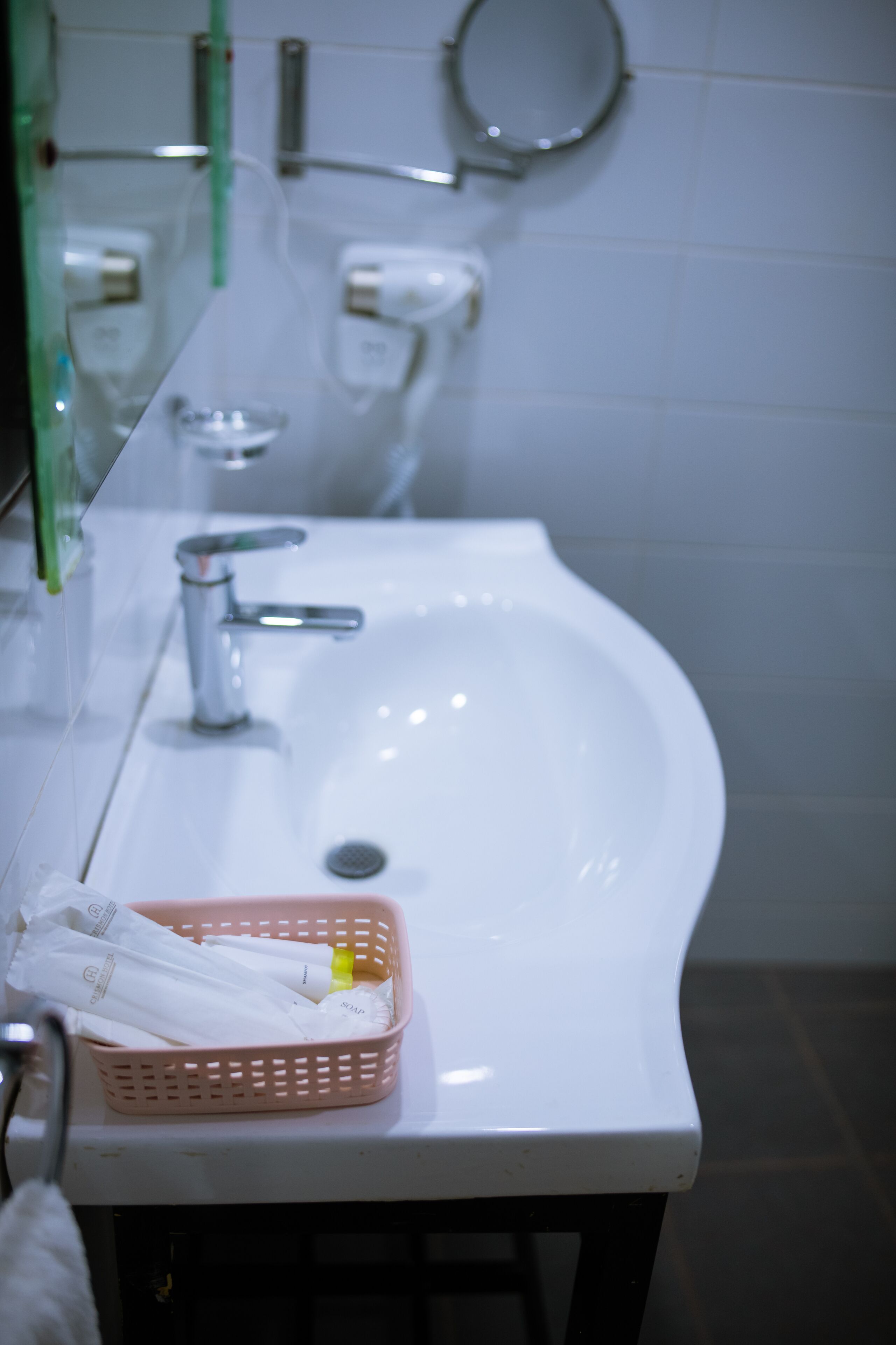 Un baño con un lavamanos blanco, un espejo y una cesta rosa con artículos de aseo.