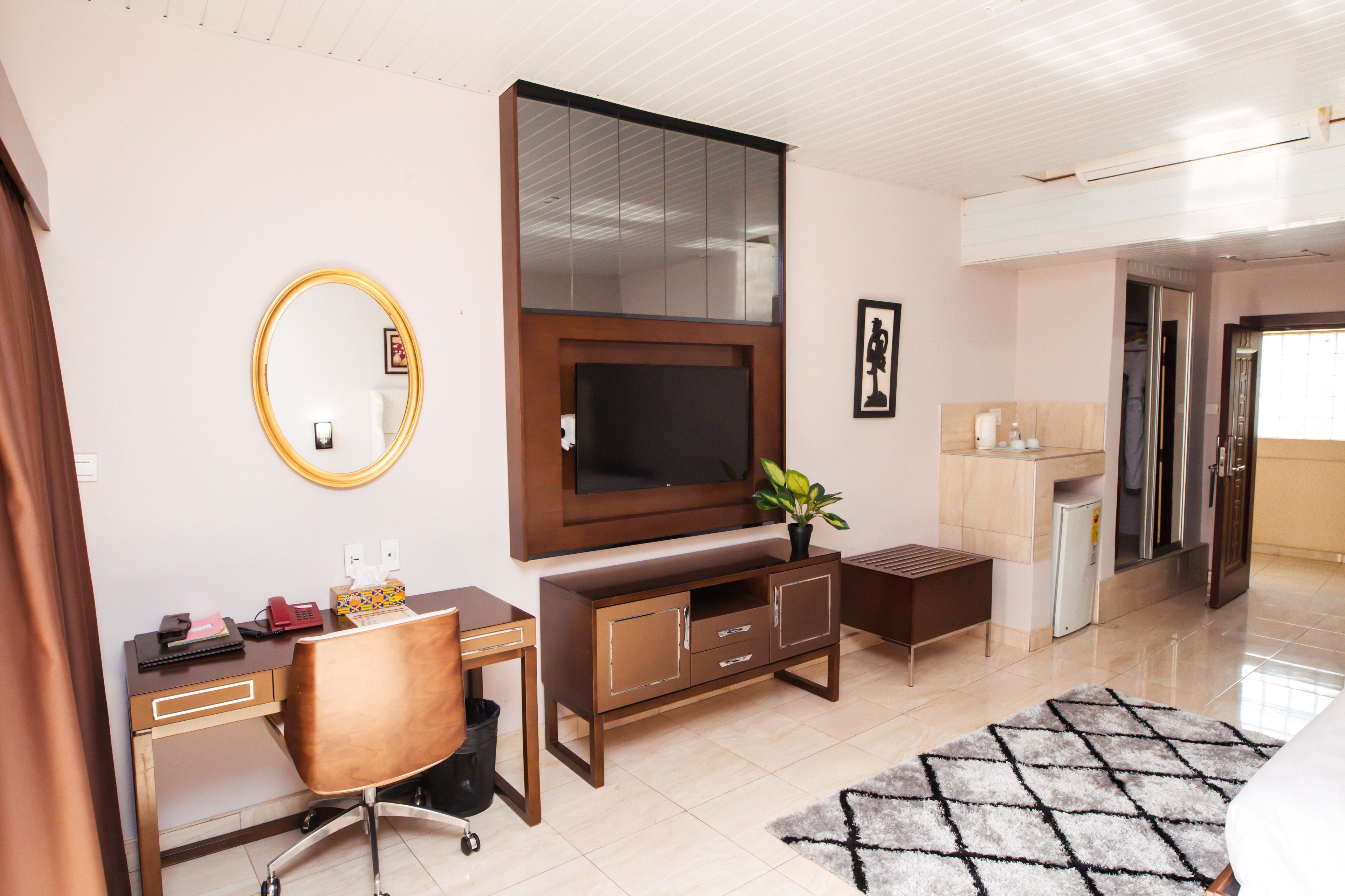 A modern living room with a TV, a desk, a chair, a small cabinet, and a potted plant.
