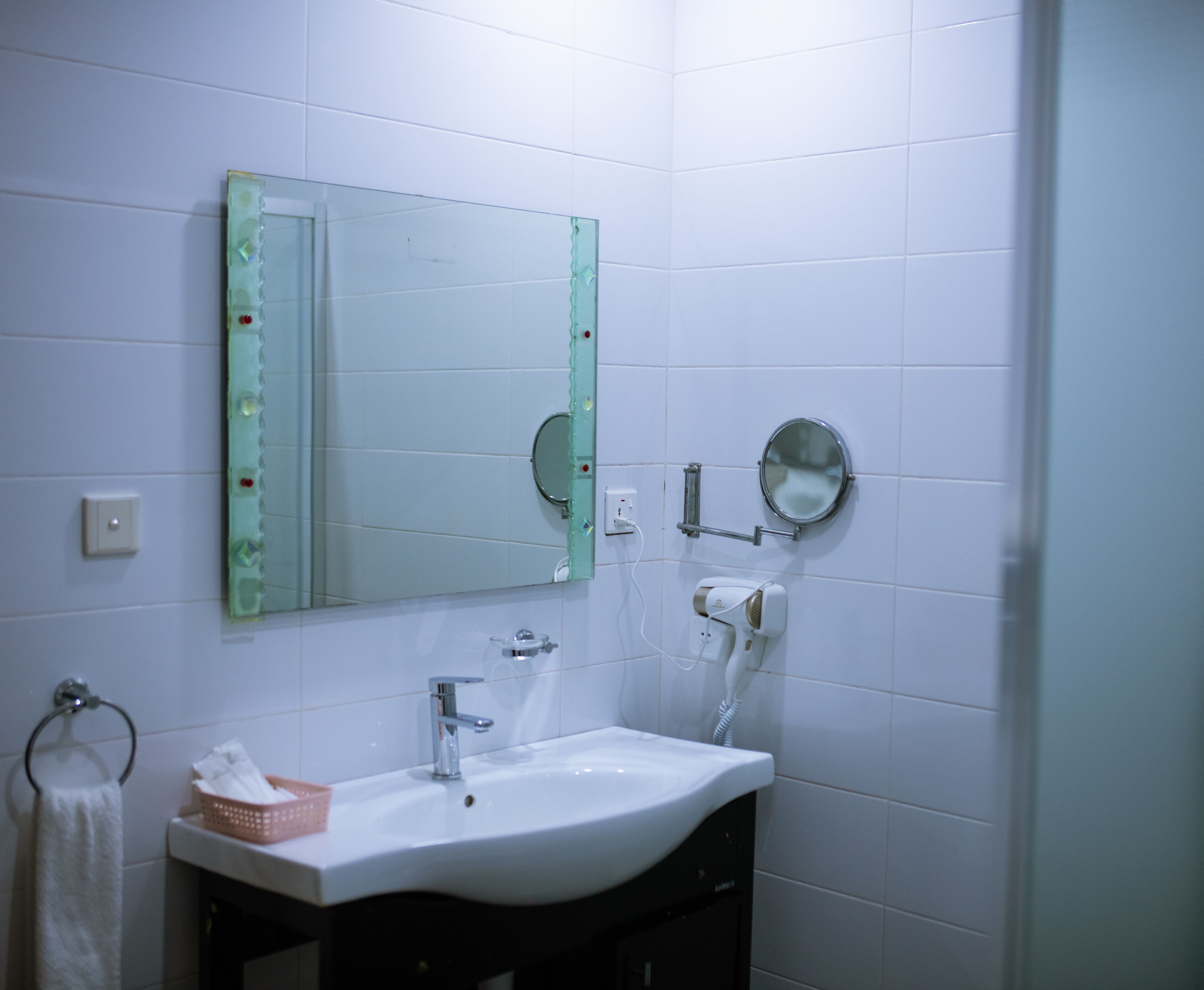 Un baño con un lavamanos blanco, un espejo y un perchero para toallas.